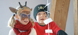 Zwei Kinder sitzen nebeneinander. Das linke Kind ist als Reh verkleidet. Vor ihnen hängen Zettel an einem Wollfaden.