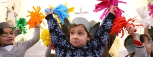 Kinder tanzen mit bunten Pompoms. Sie tragen selbstgebastelte Mäuseohren auf dem Kopf.