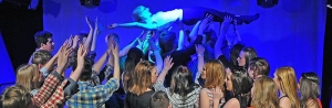 Eine junge Frau macht Stage-Diving über einer Gruppe von Schüler*innen.