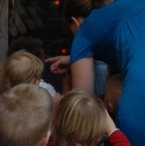 Kinder und eine Frau von hinten. Die Frau deutet mit dem Finger in eine Richtung.