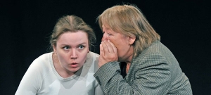 Eine Frau flüstert einer anderen Frau etwas ins Ohr. Die andere Frau schaut erschrocken.
