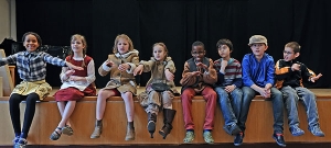 Viele Kinder sitzen nebeneinander am Rand einer Bühne.