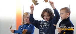 Drei Kinder stehen nebeneinander und halten Laubblätter in ihren Händen.