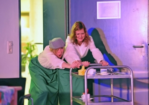 Zwei Frauen schieben mit viel Kraft einen Servierwagen in den Raum.