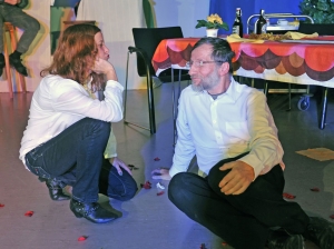 Eine Frau und ein Mann hocken auf dem Boden und schauen sich verliebt an. Die Frau deutet einen Kussmund an.