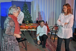 Zwei Frauen stehen sich feindselig gegenüber. Im Hintergrund stehen ein gedeckter Esstisch und ein Weihnachtsbaum. Ein Mann sitzt auf dem Esstisch, ein weiterer hockt davor.