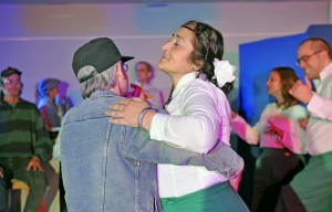 Ein Mann und eine Frau tanzen miteinander. Um sie herum stehen weitere Personen.