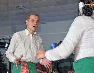 Ein Mann und eine Frau stehen sich gegenüber und schauen sich erschrocken an. Beide tragen weiße Blusen und grüne Schürzen.