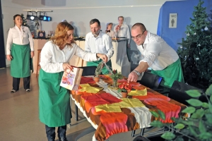 Mehrere Personen dekorieren gemeinsam einen Esstisch. Die Personen tragen weiße Hemden und grüne Schürzen.