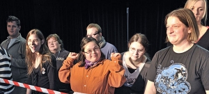 Menschen mit und ohne Behinderung stehen hinter einem Absperrband.