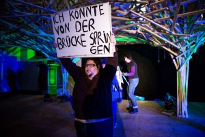 Ein Mann hält ein Schild hoch. Auf dem Schild steht: "Ich könnte von der Brücke springen".