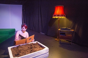 Eine junge Frau sitzt auf einer Bühne an einem Sandkasten. Sie blättert durch ein Fotobuch.