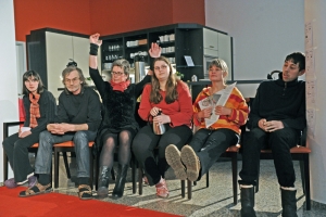 Viele Personen sitzen nebeneinander auf Stühlen. Eine Frau reckt die Arme in die Luft.