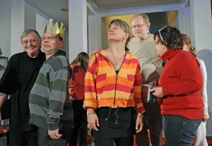 Viele Menschen stehen im Pulk zusammen. Ein Mann trägt eine goldene Papierkrone auf dem Kopf. Eine Frau hält einen Topf in der Hand.