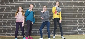 Vier Mädchen stehen vor einer Mauer und posieren lachend.