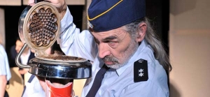 n Mann in blauer Uniform inspiziert ein geöffnetes Waffeleisen. Er hält eine Rolle rotes Absperrband in der Hand.
