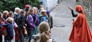 Eine Frau im Kostüm spricht mit einer Gruppe von Schulkindern.