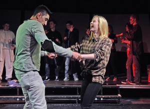 Ein Mann und eine Frau tanzen gemeinsam auf der Bühne. Die Frau lacht. Im Hintergrund stehen weitere Personen.