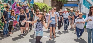 Viele Personen laufen gemeinsam durch eine Hildesheimer Gasse. Links befindet sich eine Wand mit Graffities. Im Hintergrund sieht man den Club "Thav". Die Personen werden von einer Frau angeführt, die mit ausladenden Gesten etwas erklärt.