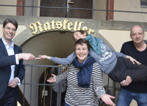 Vier Personen befinden sich vor dem Ratskeller in Hildesheim: Der Oberbürgermeister von Hildesheim, Ingo Meyer, die Geschäftsführerin des TPZ, Katrin Löwensprung, und zwei Theaterpädagogen und -pädagoginnen vom TPZ. Katrin Löwensprung und der Theaterpädagoge tragen die andere Theaterpädagogin. Der Bürgermeister trägt einen Anzug und übergibt einen Schlüssel an die drei Personen vom TPZ.