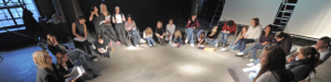 Viele junge Menschen sitzen und stehen im Kreis. Einige Menschen schreiben Notizen auf Papier.