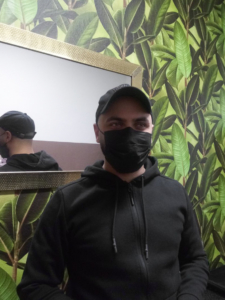 Ein Mann steht mit dem Rücken zu einem Spiegel. Er trägt eine schwarze Corona-Maske.