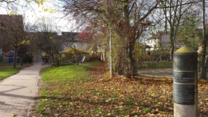 Ein Weg führt durch einen Park. Die Sonne scheint. Im Hintergrund sieht man einen Spielplatz.
