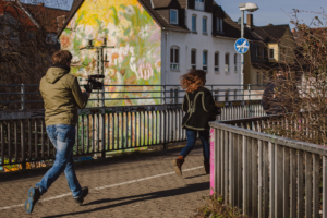 Zwei Personen rennen über eine Brücke. Die hintere Person trägt eine Kamera.