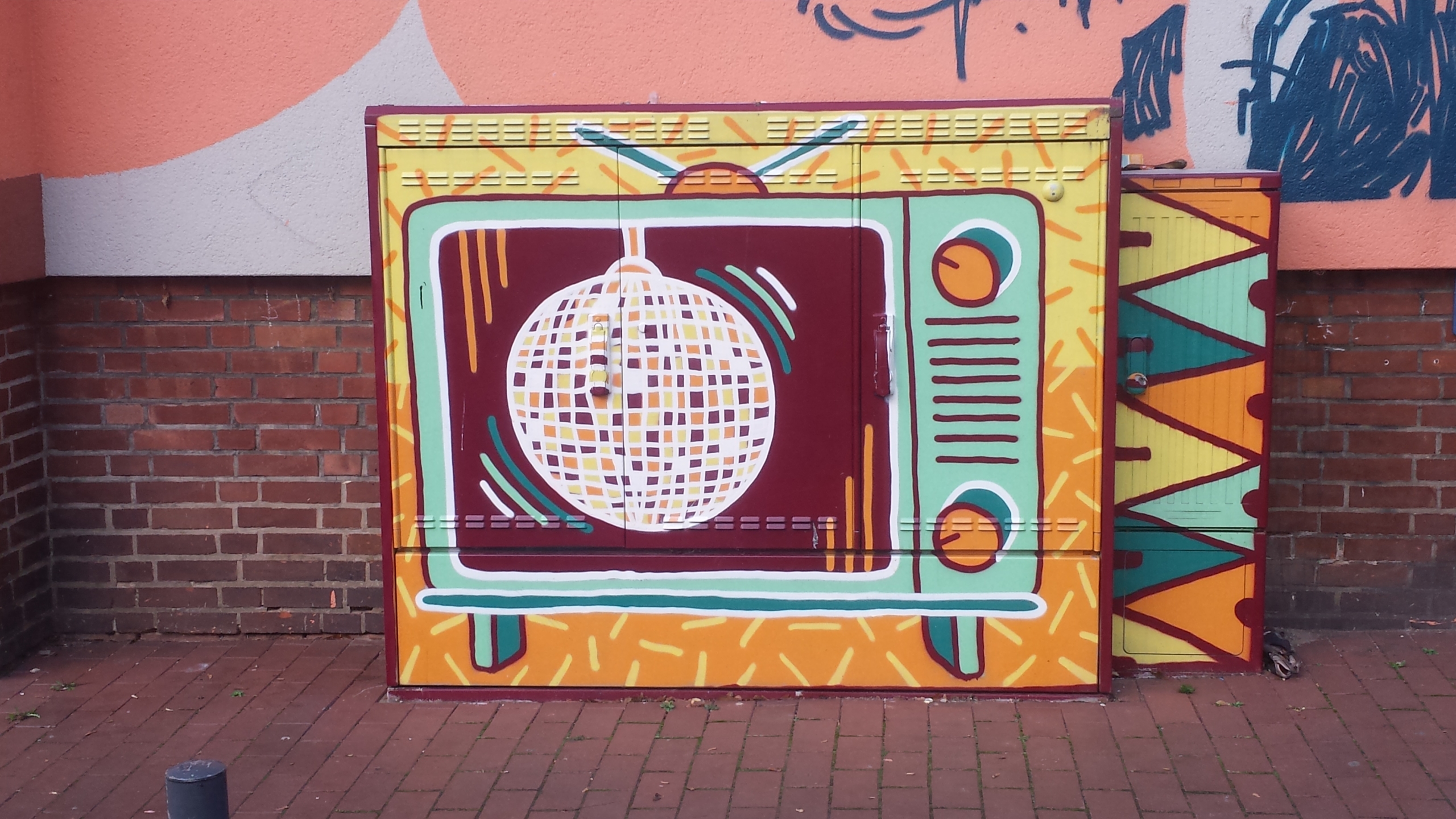 Ein Stromkasten, auf dem ein Fernseher gemalt ist. Im Fernseher sieht man eine Diskokugel.