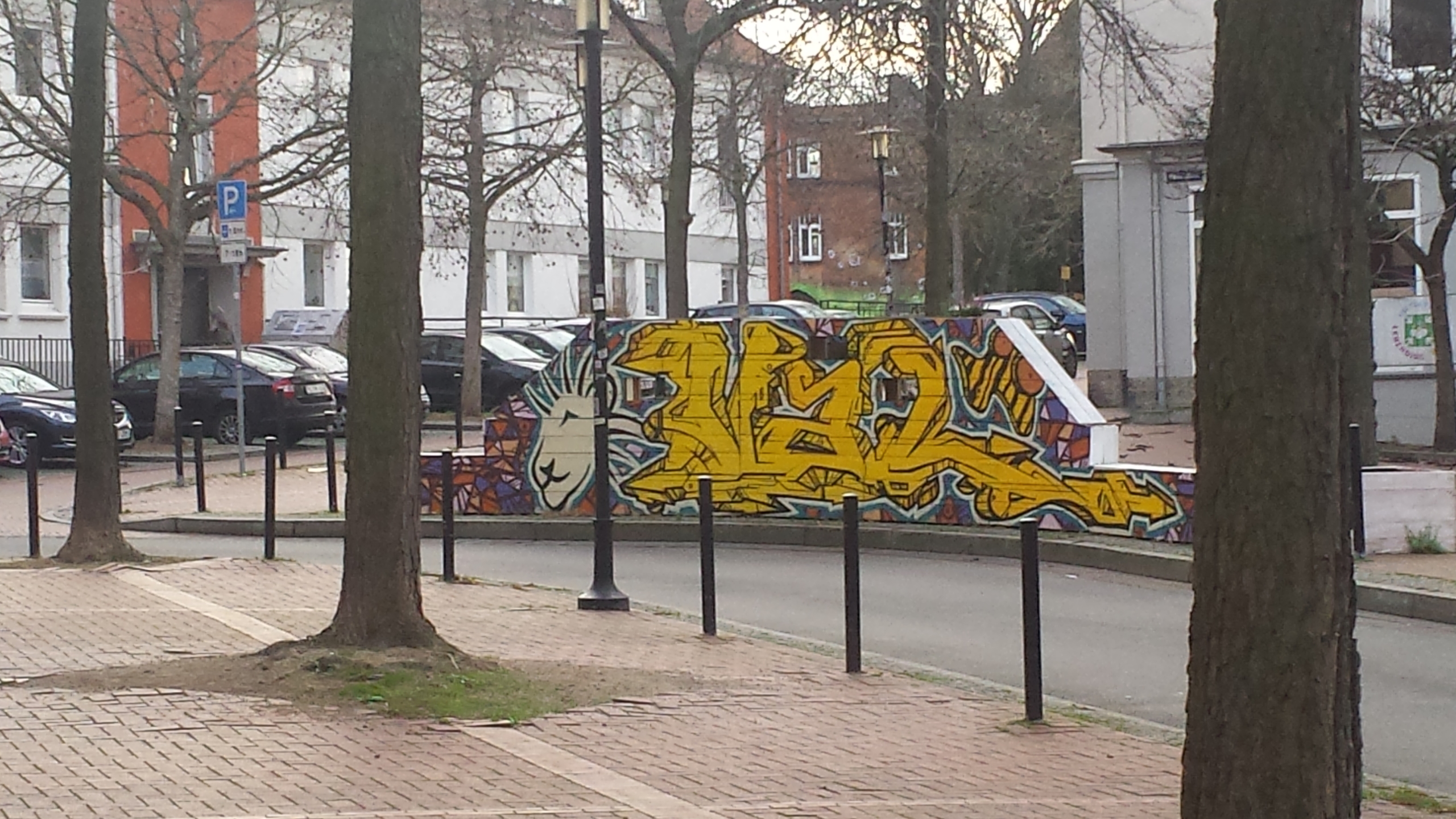 Ein Platz in Hildesheim. Im Hintergrund sind parkende Autos zu sehen. Eine Wand mit Graffities steht im Mittelpunkt.