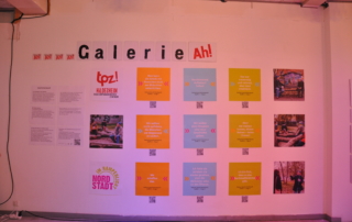 Fotos und Zitate hängen aufgereiht an einer Wand. Darüber steht der Schriftzug: "Galerie Ah!"