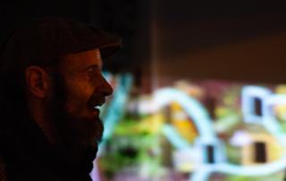 Ein Mann ist aus der Seitenansicht zu sehen. Hinter ihm befinden sich bunte Lichter.