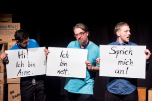Drei Männer in blauen T-Shirts stehen nebeneinander. Sie halten Schilder in die Kamera. Das erste Schild trägt die Aufschrift: "Hi! Ich bin Arne." Auf dem zweiten Schild steht: "Ich bin nett." Auf dem dritten Schild steht: "Sprich mich an!"