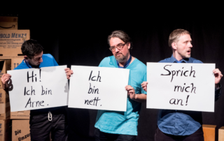 Drei Männer in blauen T-Shirts stehen nebeneinander. Sie halten Schilder in die Kamera. Das erste Schild trägt die Aufschrift: "Hi! Ich bin Arne." Auf dem zweiten Schild steht: "Ich bin nett." Auf dem dritten Schild steht: "Sprich mich an!"