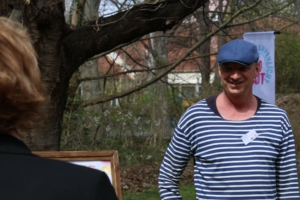 Ein Mann in gestreiftem Shirt lächelt in die Kamera. Vor ihm ist eine weitere Person von hinten zu sehen.