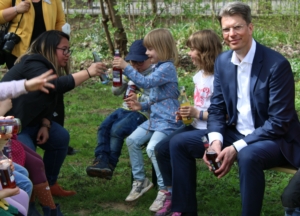 Der Oberbürgermeister von Hildesheim, Ingo Meyer, sitzt auf einer Bank und blickt in die Kamera. Die Bank steht auf einer Wiese. Neben dem Bürgermeister sitzen Kinder und trinken Limo.