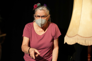 Eine Frau in rosa T-Shirt zeigt mit strengem Blick in Richtung unterhalb des Bildes.