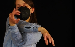 Eine junge Frau tanzt vor einem schwarzen Hintergrund.