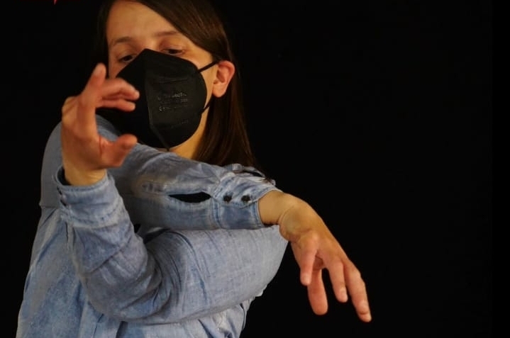 Eine junge Frau tanzt vor einem schwarzen Hintergrund.