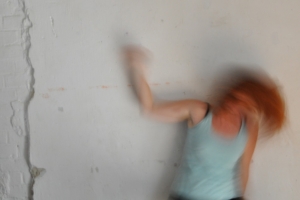 Eine Frau mit roten Haaren bewegt sich schnell vor einer weißen Wand. Die Frau ist durch die Bewegung nur verschwommen zu sehen.