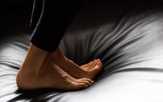 Die nackten Füße einer Frau stehen auf einem schwarzen Ledersofa.