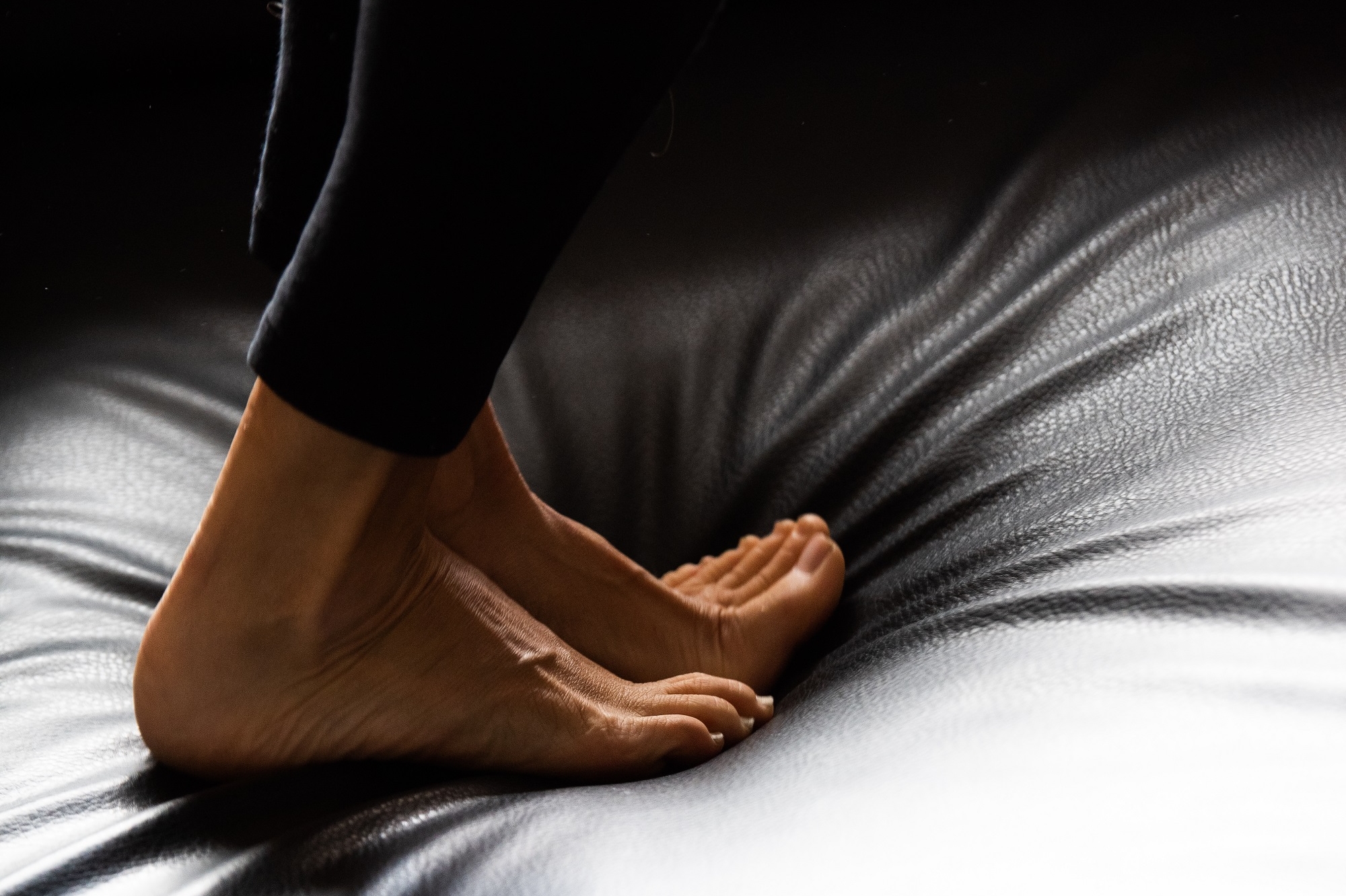 Die nackten Füße einer Frau stehen auf einem schwarzen Ledersofa.