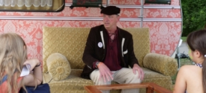 Ein Mann sitzt auf dem Sofa und erzählt eine Geschichte. Zwei Personen hören zu.