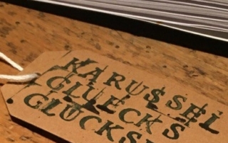 Auf einem Holztisch liegen braune Zettel. Auf den Zetteln stehen Worte: "Woll-Socken-Wonne" und "Schnee-Flocken-Flüstern".