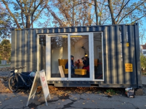 Zwei Personen sitzen in einem Schiffscontainer und unterhalten sich.