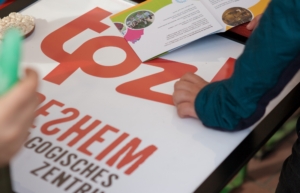 Das Logo vom TPZ liegt eingerahmt auf einem Tisch. Kinderhände sind im Bild zu sehen.