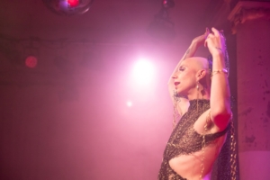 Eine Drag-Person lehnt sich mit dem Rücken an eine Wand. Das Foto ist in rosa Licht getaucht.