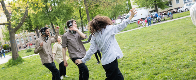 Menschen tanzen mit Kopfhörern auf den Ohren durch den Park.