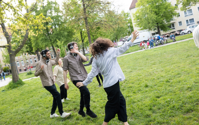 Menschen tanzen mit Kopfhörern auf den Ohren durch den Park.