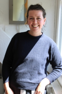 Eine Frau lehnt am Fenster und lächelt in die Kamera.